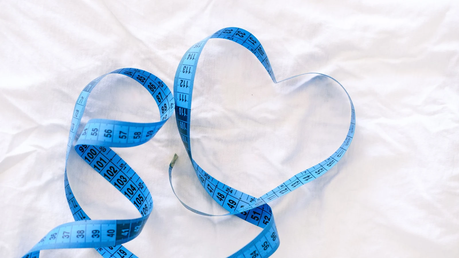 Blue measuring tape forming a heart on white fabric, symbolizing love and measurements. — selected for United States readers