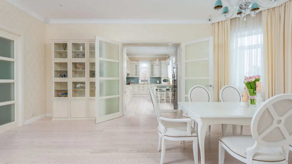 Interior of spacious light dining room with white table and cozy chairs near large window with curtains — selected for United Kingdom readers