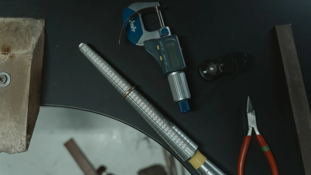 A collection of jewelry crafting tools including a ring mandrel and caliper on a workbench. — selected for United Kingdom readers