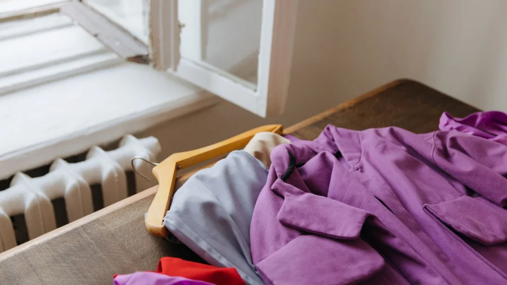 Purple coat on hanger beside open window, offering natural light and warmth. — selected for United States readers