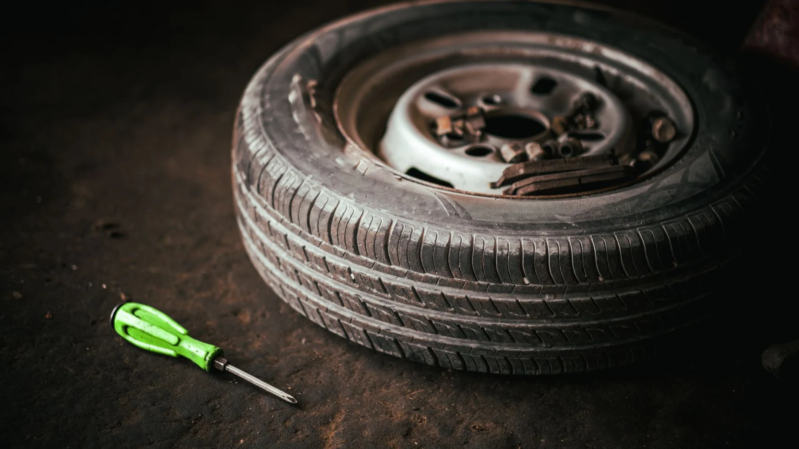 A car tire and green screwdriver placed on the garage floor, representing automotive repair. — selected for United Kingdom readers