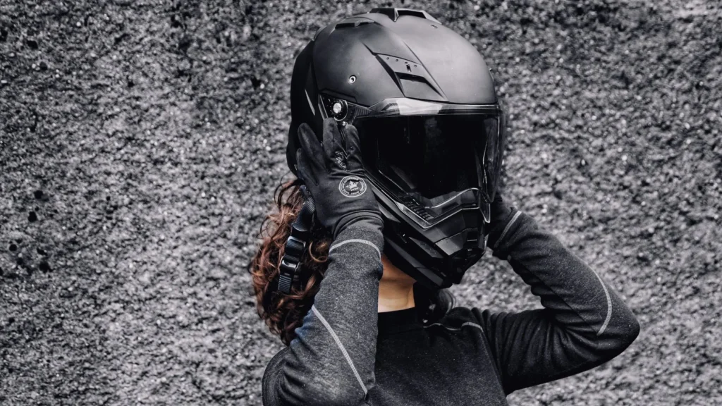 A woman in gloves putting on a motorcycle helmet against a textured background, highlighting safety and adventure. — selected for United States readers