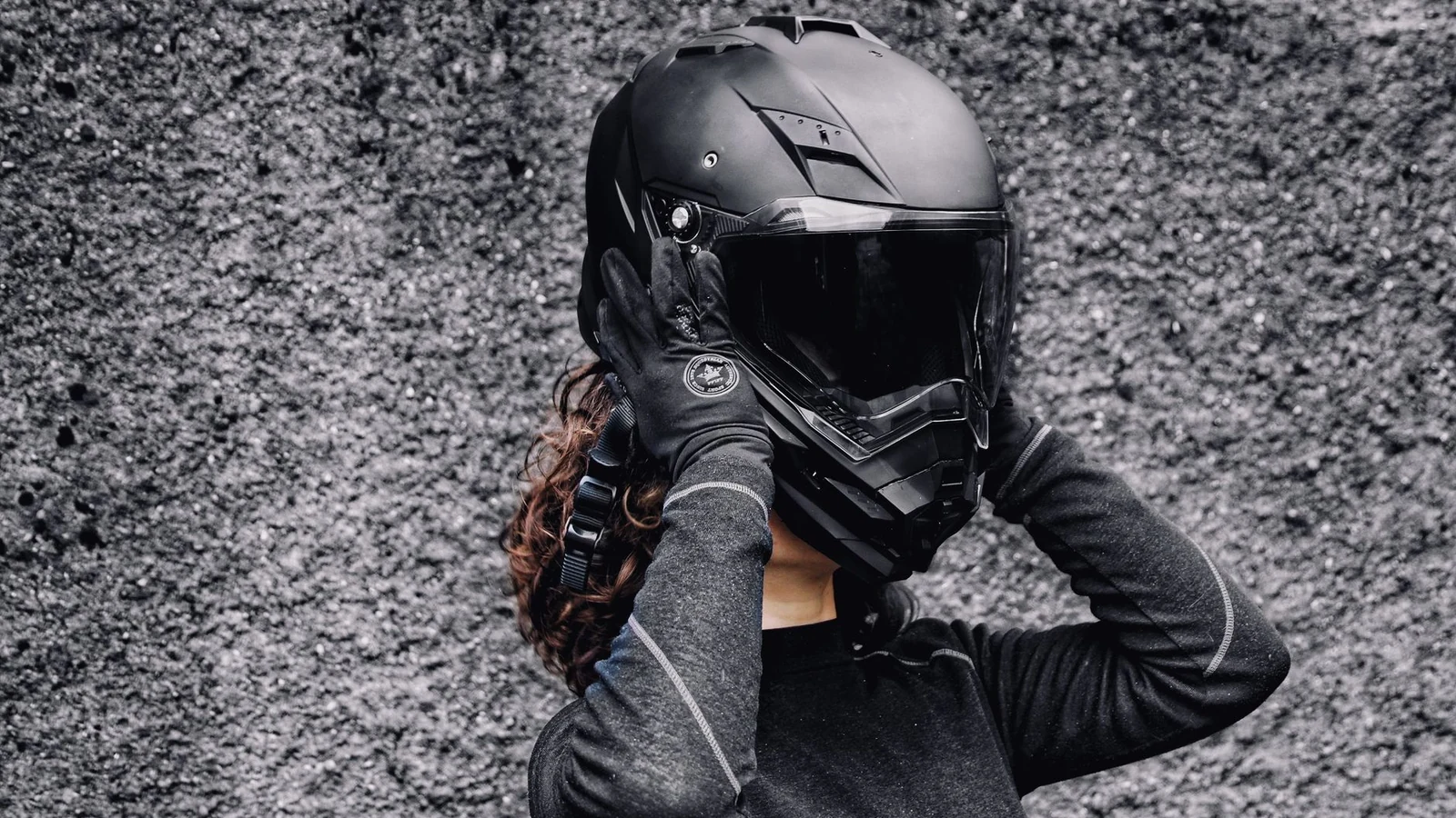A woman in gloves putting on a motorcycle helmet against a textured background, highlighting safety and adventure. — selected for United States readers