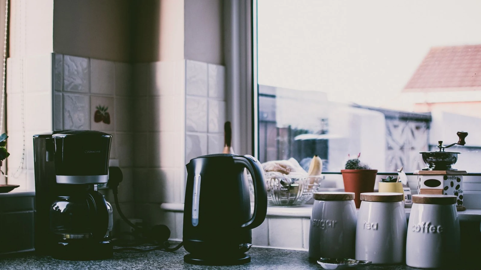Cozy kitchen scene with coffee maker, kettle, and jars on a sunny counter. — selected for United States readers