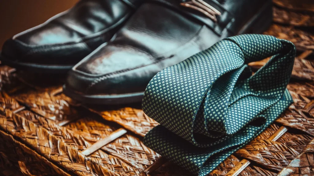 Close-up of a stylish necktie and polished leather shoes resting on a woven wicker surface. — selected for United States readers