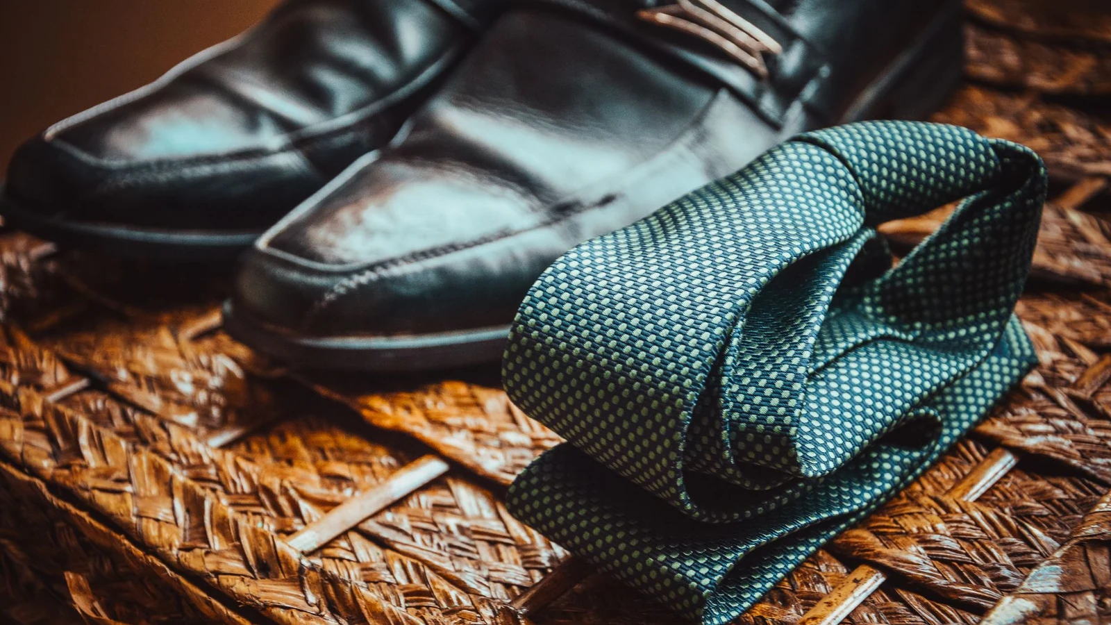 Close-up of a stylish necktie and polished leather shoes resting on a woven wicker surface. — selected for United States readers