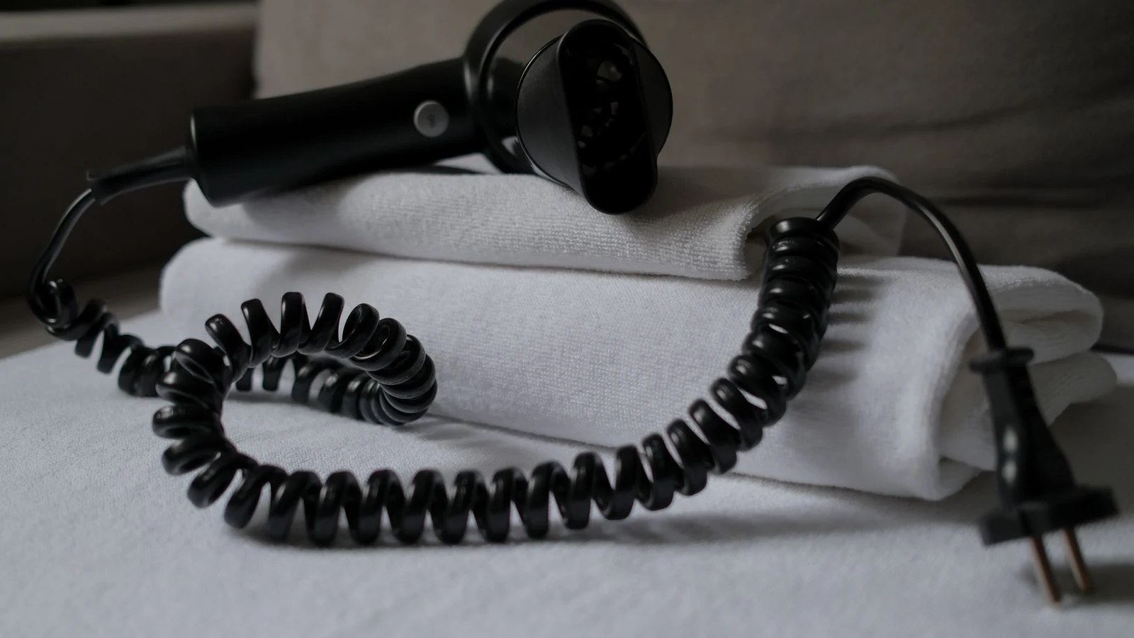 A coiled hair dryer placed on folded white towels, suggesting a hotel setting. — selected for United Kingdom readers
