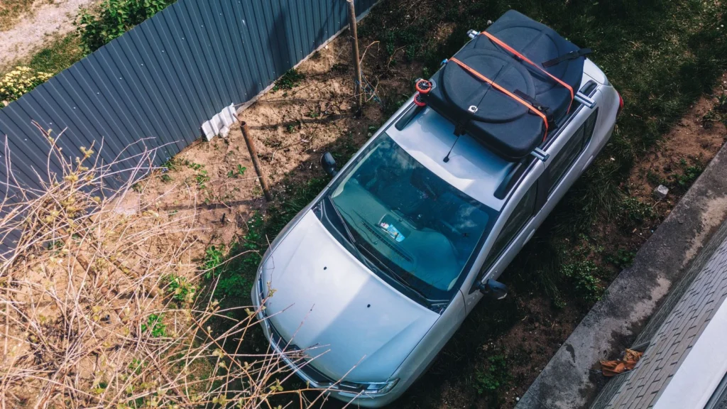Aerial view of a silver car parked with a roof cargo carrier in a garden setting under clear daylight. — selected for United Kingdom readers
