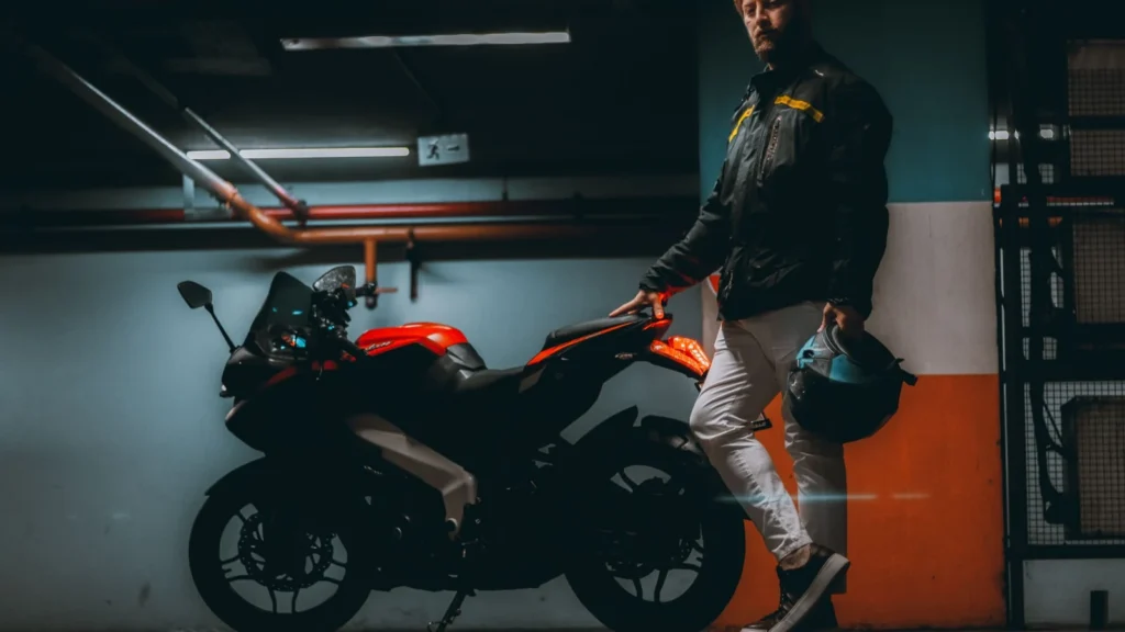 A man holds a helmet beside his motorcycle in a dimly lit garage. — selected for United States readers