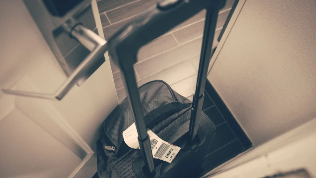 Travel suitcase with tag by hotel door, symbolizing travel or business trip. — selected for United States readers