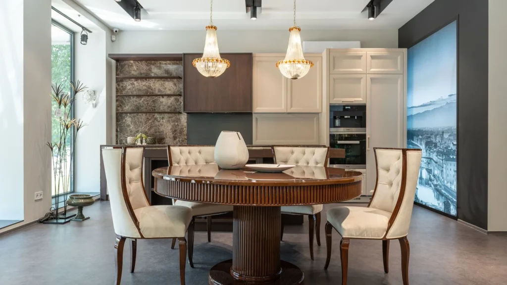 Interior of elegant spacious kitchen with wooden furniture and shiny crystal chandelier hanging over dining zone with round table and comfortable chairs — selected for United Kingdom readers