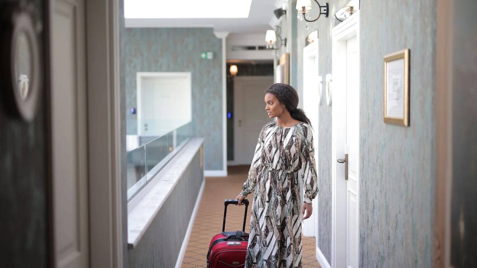 A woman walks with luggage through a stylish hotel corridor, embodying travel elegance. — selected for United States readers