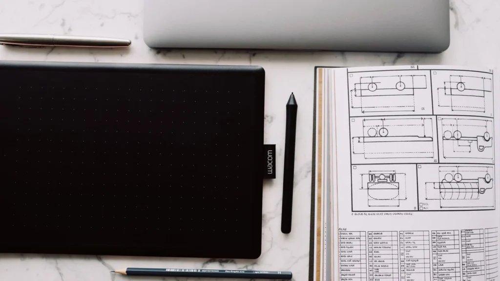From above of opened sketchbook with drawn scheme and tablet with black screen located near sharp pencil and marker — selected for United States readers