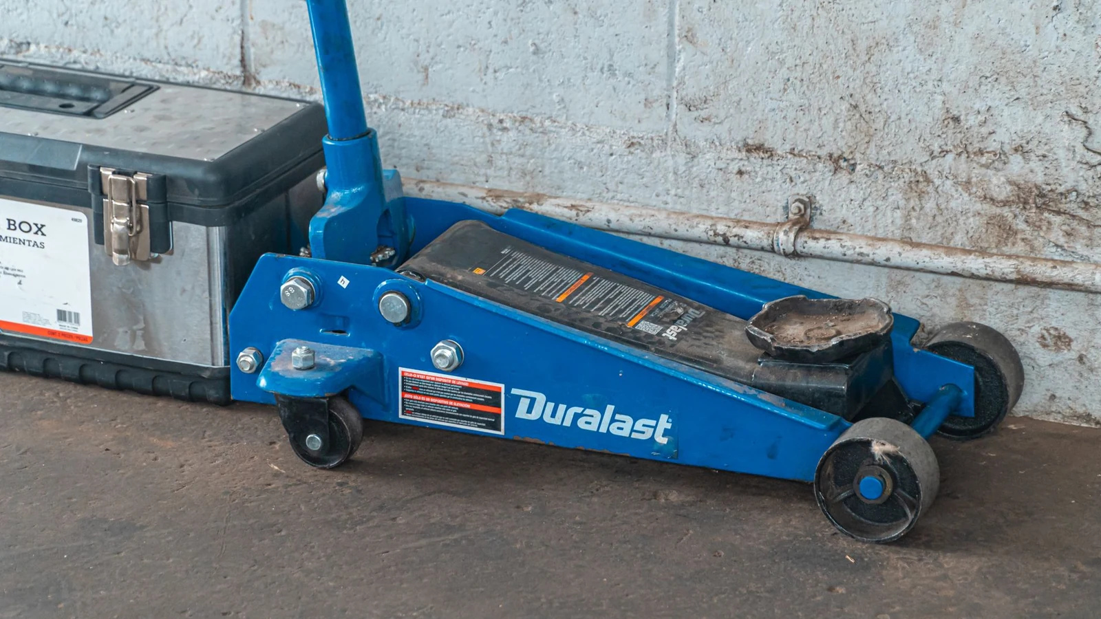A blue hydraulic floor jack with a toolbox in an automotive garage setting. — selected for United Kingdom readers