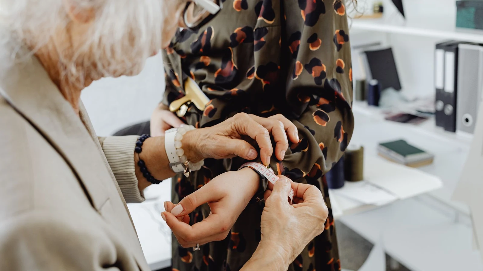 Elderly tailor taking dress measurements on a young woman in a fashion studio. Professional attire fitting. — selected for United States readers