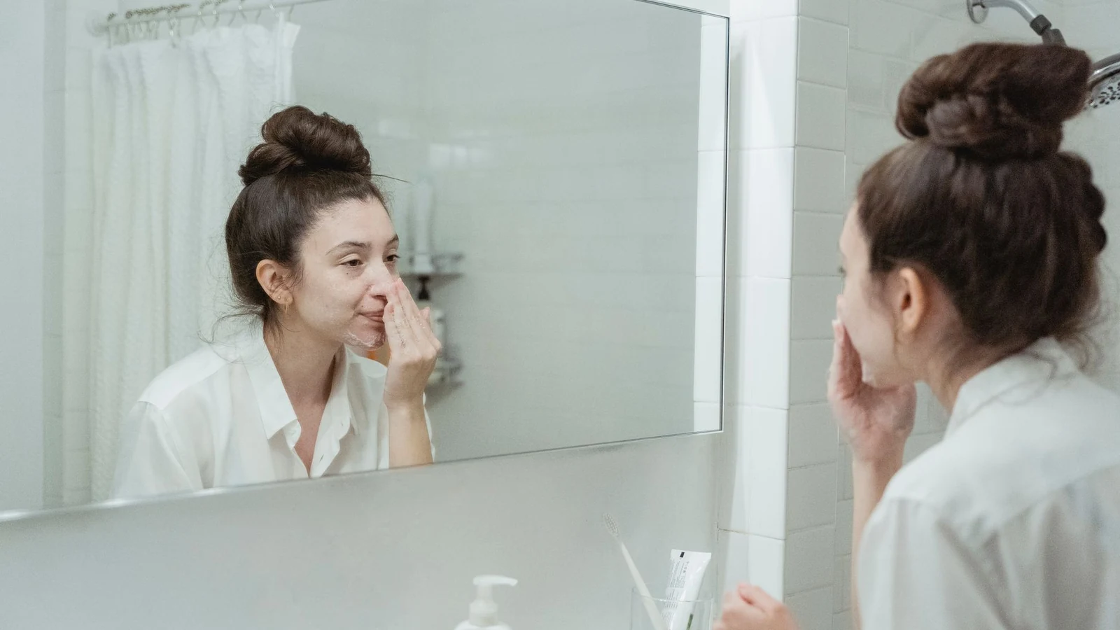 Caucasian woman in bathroom applying skincare product while looking in the mirror. — selected for United Kingdom readers