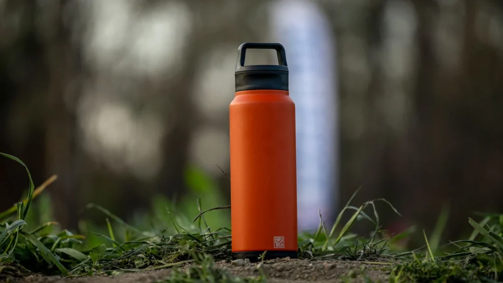 A vibrant orange water bottle sits on grass in an outdoor setting, perfect for hiking and adventures. — selected for United Kingdom readers
