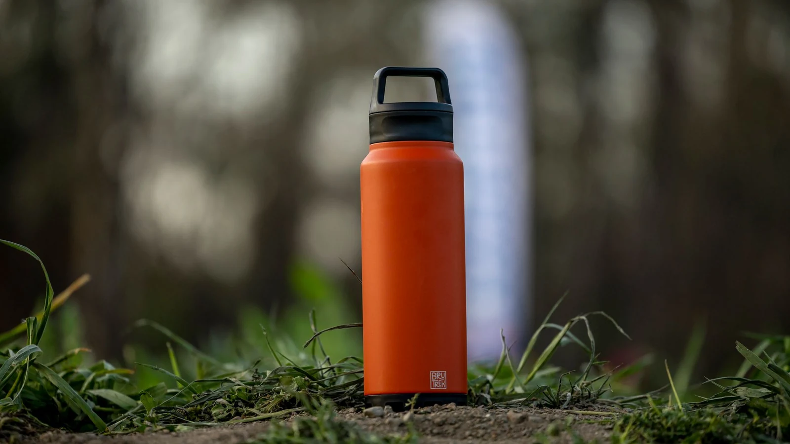 A vibrant orange water bottle sits on grass in an outdoor setting, perfect for hiking and adventures. — selected for United Kingdom readers