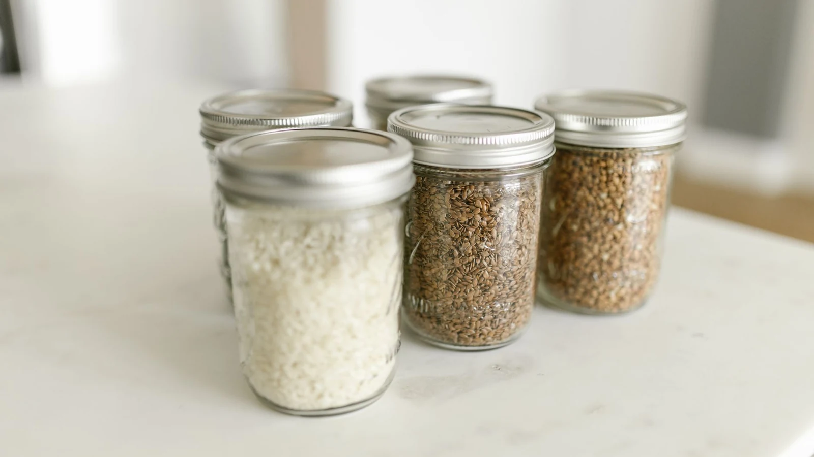 Close-up of glass jars filled with rice and grains on a kitchen counter, ideal for storage. — selected for United States readers