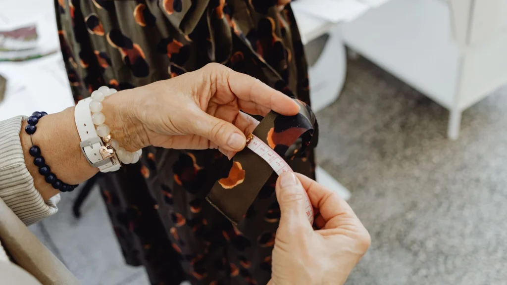 Detailed close-up of seamstress' hands measuring fabric with tape in a fashion studio setting. — selected for United States readers
