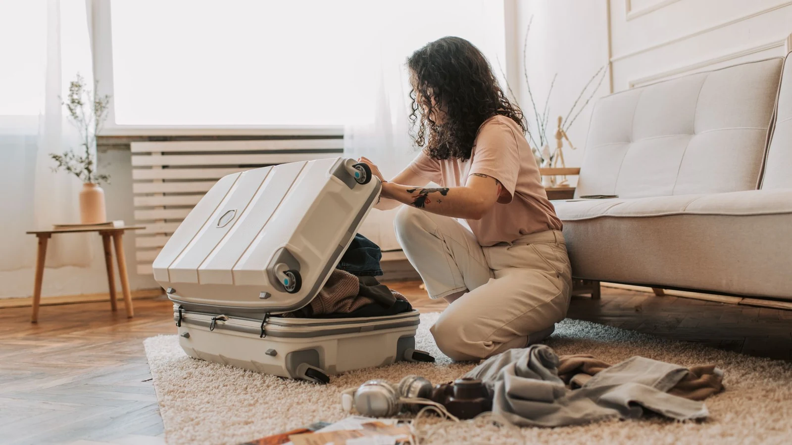A woman packing her suitcase in a stylish living room, surrounded by clothes and travel accessories. — selected for United States readers